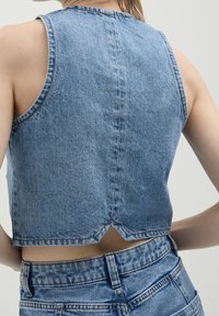 Blå denimkort väst med hög krage, ärmlös design och delad rygg. Kännetecknas av sin textur och synliga söm detaljer.