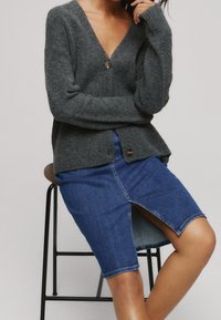 Grå ullkofta med V-ringning och enkel knappstängning; matchas med en blå denimpennkjol med en framtill slit och rå fåll.