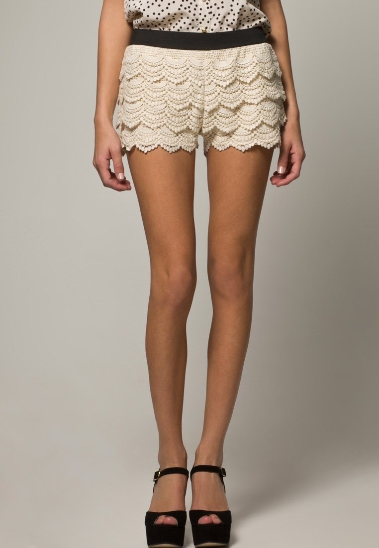 Krämfärgade virkade shorts med ett vågigt mönster och ett svart elastiskt midjeband, tillsammans med högklackade svarta skor.