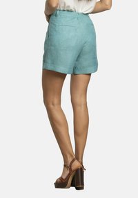 Pantalones cortos de lino de color aqua con un ajuste relajado, dobladillos enrollados y bolsillos traseros, combinados con sandalias de tacón alto marrones con tirantes.