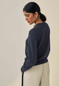 Pullover blu navy con scollatura rotonda, maniche a palloncino e orlo a costine. Abbinato a pantaloni chiari, realizzati in un tessuto morbido.