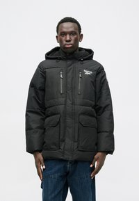 Musta puhvijakku irrotettavalla hupulla, kaksi rintataskua ja kaksi etutaskua. Sisältää Reebok-logon ja vetoketjusulkimet.