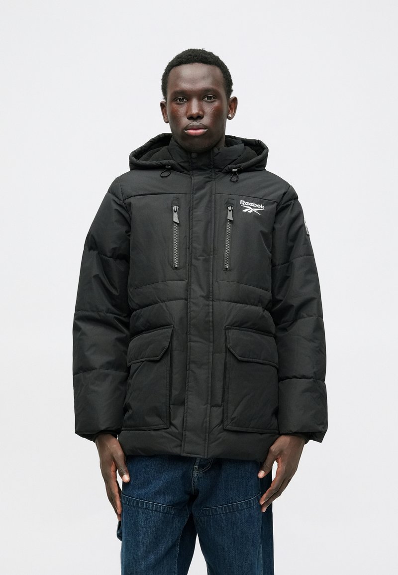 Musta puhvijakku irrotettavalla hupulla, kaksi rintataskua ja kaksi etutaskua. Sisältää Reebok-logon ja vetoketjusulkimet.