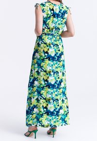 Maxime mekko, jossa on sininen, vihreä ja valkoinen kukkakuosi. Varustettu hihattomilla hihoilla ja istuvalla vyötäröllä. Yhdistetty vihreisiin koroke kenkiin.