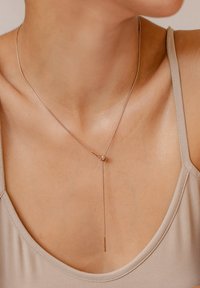 Collar de oro rosa con una cadena delgada, que presenta una cuenta redonda y un colgante recto, suspendido sobre un fondo neutro.