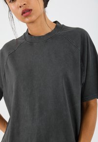 Overly grote zwarte katoenen t-shirt met een ronde hals, korte raglanmouwen en een zachte, gestructureerde afwerking. Heeft een relaxte pasvorm en minimale details.
