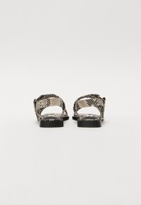 Snake-print sandals with flat black soles, open backs, and woven straps. Texture features a reptile pattern and a smooth finish.