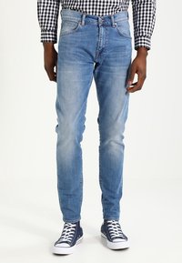 Light blue denim jeans with a slim fit, featuring front pockets and a mid-rise waist. Paired with blue low-top sneakers.