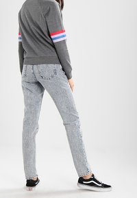 Grijze sweatshirt met meerkleurige strepen op de mouwen, lichtgrijze jeans met hoge taille en zwarte sneakers met witte zolen.