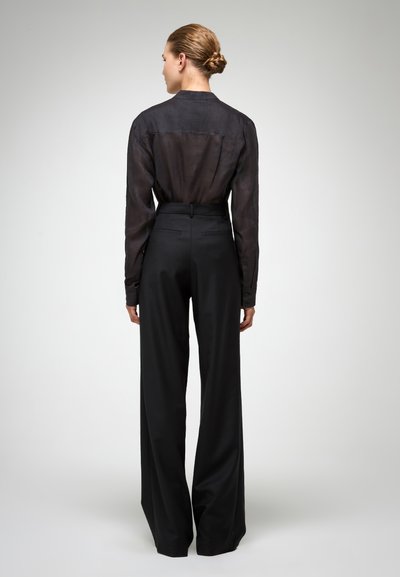 Blouse noire transparente avec une silhouette droite et des manches longues, associée à un pantalon large taille haute noir. Texture lisse, détails minimaux.