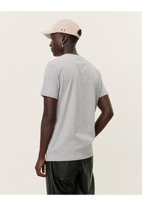 Camiseta de algodón gris con mangas cortas, llevada con una gorra beige, combinada con pantalones de cuero negros. Diseño simple sin patrones visibles.