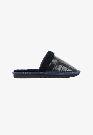 Chausson en cuir noir à texture crocodile, doublure polaire bleu marine et bordure de semelle, marqué "Chloé" sur le bord de la semelle.