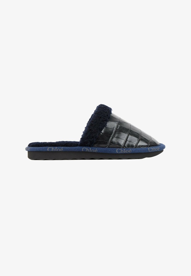 Chausson en cuir noir à texture crocodile, doublure polaire bleu marine et bordure de semelle, marqué "Chloé" sur le bord de la semelle.