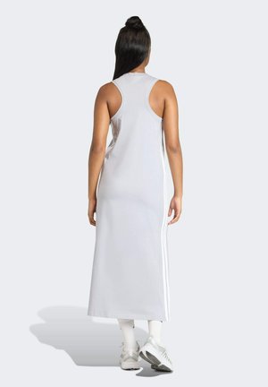 Szara sukienka bez rękawów o długiej sylwetce, z białymi bocznymi paskami i gładką fakturą materiału. Noszona z białymi skarpetkami i butami.