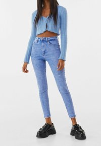 Lichtblauwe cropped trui met geribbelde textuur, gecombineerd met lichtblauwe high-waisted skinny jeans. Zwarte chunky schoenen maken de outfit compleet.