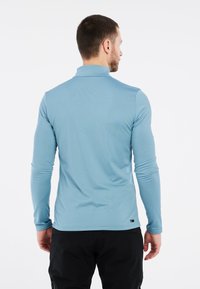 Šviesiai mėlyna ilgomis rankovėmis marškiniai su apykakle, lygus paviršius ir prigludusi forma. Priede yra mažas prekės ženklas etiketė isteigabalai.