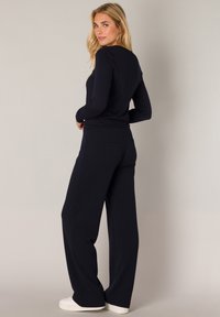 Marineblauwe top met lange mouwen en bijpassende wijde broek. Glad materiaal, getailleerde pasvorm, geen zichtbare patronen. Witte sneakers maken de outfit compleet.