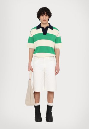 Gestreepte polo in groen, wit en marineblauw; witte shorts; zwarte enkelbooties; houdt een beige schoudertas vast. Eenvoudig ontwerp, relaxte pasvorm.