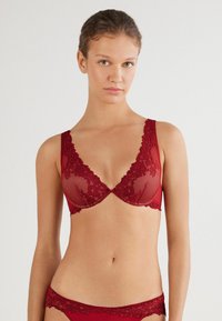Czerwony koronkowy stanik z głębokim dekoltem, kwiatowym wzorem i regulowanymi ramiączkami. Miękka siateczka z koronką oraz gładki tył.