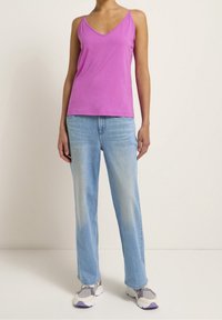 Lila ärmlös topp med v-ringning, kombinerad med ljusblå raka jeans och grå sneakers med lila detaljer.