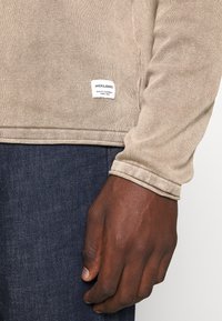 Bežna pulover izrađena od teksturiranog materijala, sa jednim bočnim etiketa s logotipom "JACK & JONES", u kombinaciji s tamnoplavim trapericama.