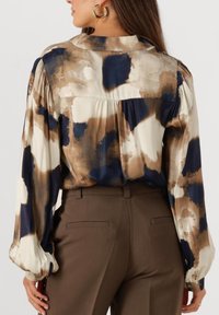 Multicolored blouse with abstract watercolor pattern in beige, navy, and brown. Features puffed sleeves and a gathered back seam.