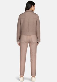 Veste courte en mélange de laine marron avec un col structuré et des détails de boutons, associée à un pantalon ajusté beige clair et des baskets blanches.