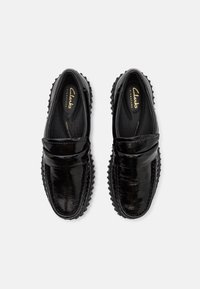 Mocassins en cuir noir avec une finition brillante, dotés d'une couture, d'un col rembourré et d'une semelle en caoutchouc texturée pour l'adhérence.