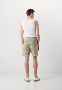 Lichtgroene badstof korte broek met verticale strepen, achterzakdetail, gecombineerd met een witte tanktop en beige sneakers.