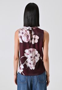 Blusa senza maniche in borgogna con grande stampa floreale in rosa e bianco. Presenta un colletto con fiocco e una texture liscia e setosa.