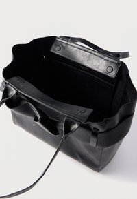 Μαύρη δερμάτινη τσάντα tote με υφή στο κάτω μέρος, λείο πάνω μέρος, μακριά χερούλια και μαγνητικό κλείσιμο. Στο εσωτερικό διαθέτει τσέπη και μαλακή επένδυση.