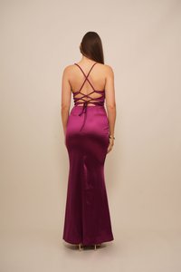 Abito lungo in satin viola, aderente, con design a incrocio sulla schiena e dettagli con lacci, caratterizzato da una texture liscia e un fondo svasato.