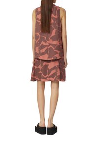 Robe sans manches, superposée, de couleur rose rouillé avec des motifs sombres abstraits. Le matériau semble léger, accompagnée de sandales à plateforme noires.