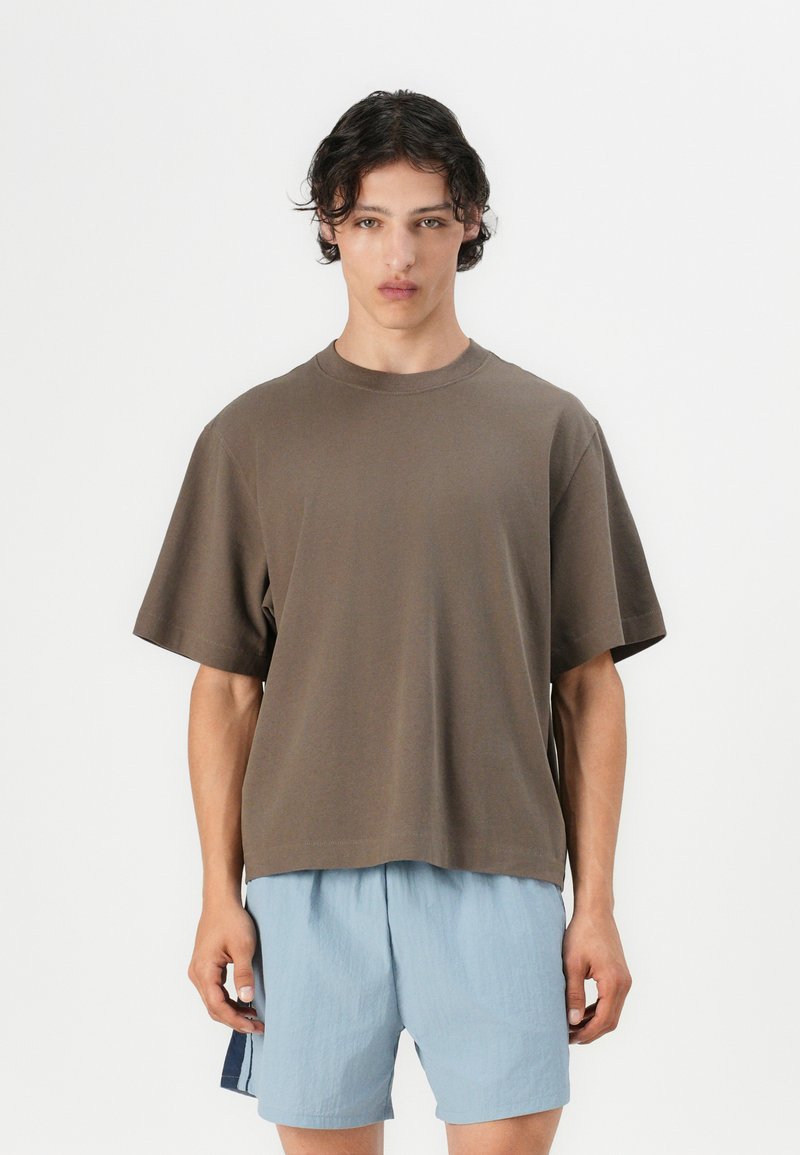 T-shirt en coton marron à manches courtes, coupe décontractée, col rond, associé à un short texturé bleu clair. Design simple et minimaliste.