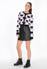 Cardigan a fantasia viola e nera con design a cuore, abbinato a una minigonna di pelle nera e stivali neri con lacci.