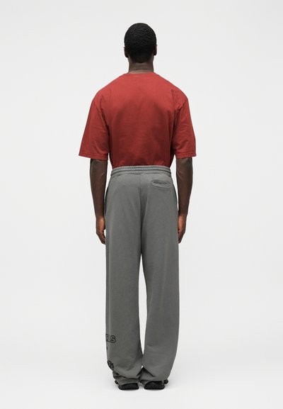 T-shirt en coton rouge à manches courtes associé à un pantalon de survêtement gris ample avec une taille élastique et une poche latérale, vu de dos.