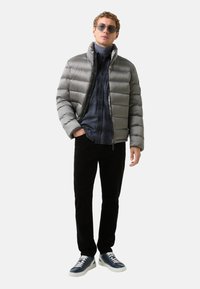 Doudoune matelassée grise, chemise écossaise bleue, pantalon en velours côtelé noir et baskets bleues avec semelles blanches. Le mannequin porte des lunettes de soleil.