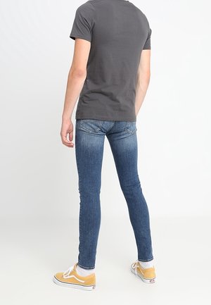 Camiseta gris, jeans ajustados azules y zapatillas amarillas. Los jeans tienen un diseño clásico con bolsillos traseros y un ligero desgastado.