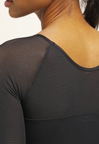 Top atlético negro con un panel de malla en el hombro, tejido texturizado y una sección inferior suave con escote redondo.