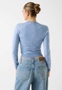 Maglione azzurro chiaro a maniche lunghe con un motivo sottile e polsini a costine. Abbinato a jeans a vita alta a lavaggio medio con una toppa logo.