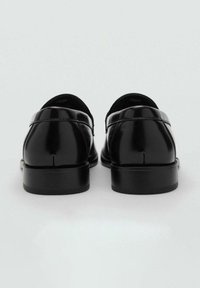 Zapatos de cuero negro con un acabado brillante, punteras redondeadas y una suela baja de goma negra. Detalle de costura discreta a lo largo de la parte trasera.