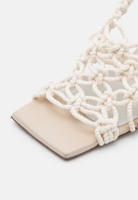 Sandale beige avec un bout carré et un design ouvert composé de larges brides en corde blanche tissée formant un motif en filet.