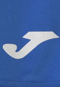 Modrá tkanina s bílým logem připomínajícím abstraktní šipku s zakřiveným zdobením, vytvářející dynamický vizuální kontrast. Texturovaný povrch.