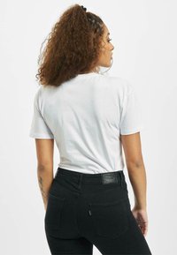 Hvit t-skjorte med kort ermer, kombinert med h�øyt liv svarte jeans. Jeansene har synlig søm og et merke på linningen.