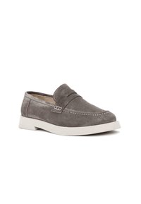 Mocasín de ante gris con suela de goma blanca plana, detalles de costura y una correa cruzada en el empeine para mayor estructura.