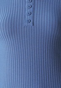 Top blu ribbed con una serie di bottoni nella parte anteriore, composto da un morbido tessuto testurizzato, caratterizzato da cinque bottoni coordinati.