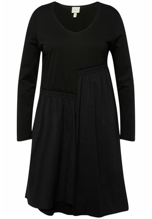 Zwarte jurk met lange mouwen, een v-hals en een elastische taille. Kenmerkt zich door een gelaagd ontwerp met contrasterende texturen en een vloeiende silhouet.