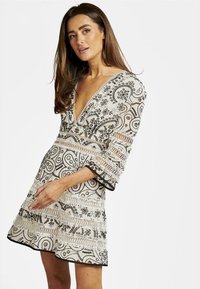 Vestido de manga corta con escote en V pronunciado en crema, con intrincados bordados florales en negro y borde de encaje, que presenta una falda de capas y una tela texturizada.
