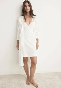 Rochie de somn albă cu decolteu în V adânc și dantelă, asociată cu un cardigan lung, ușor și asortat. Materialul pare neted, în croială lejeră.