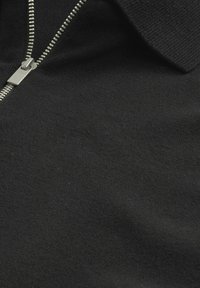 Musta vetoketjullinen vaatekappale, joka on valmistettu neulotusta kankaasta ja jossa on hopeanvärinen vetoketju ja kaulus. Tekstuuri vaikuttaa pehmeältä ja sileältä, eikä siinä ole näkyviä kuvioita.